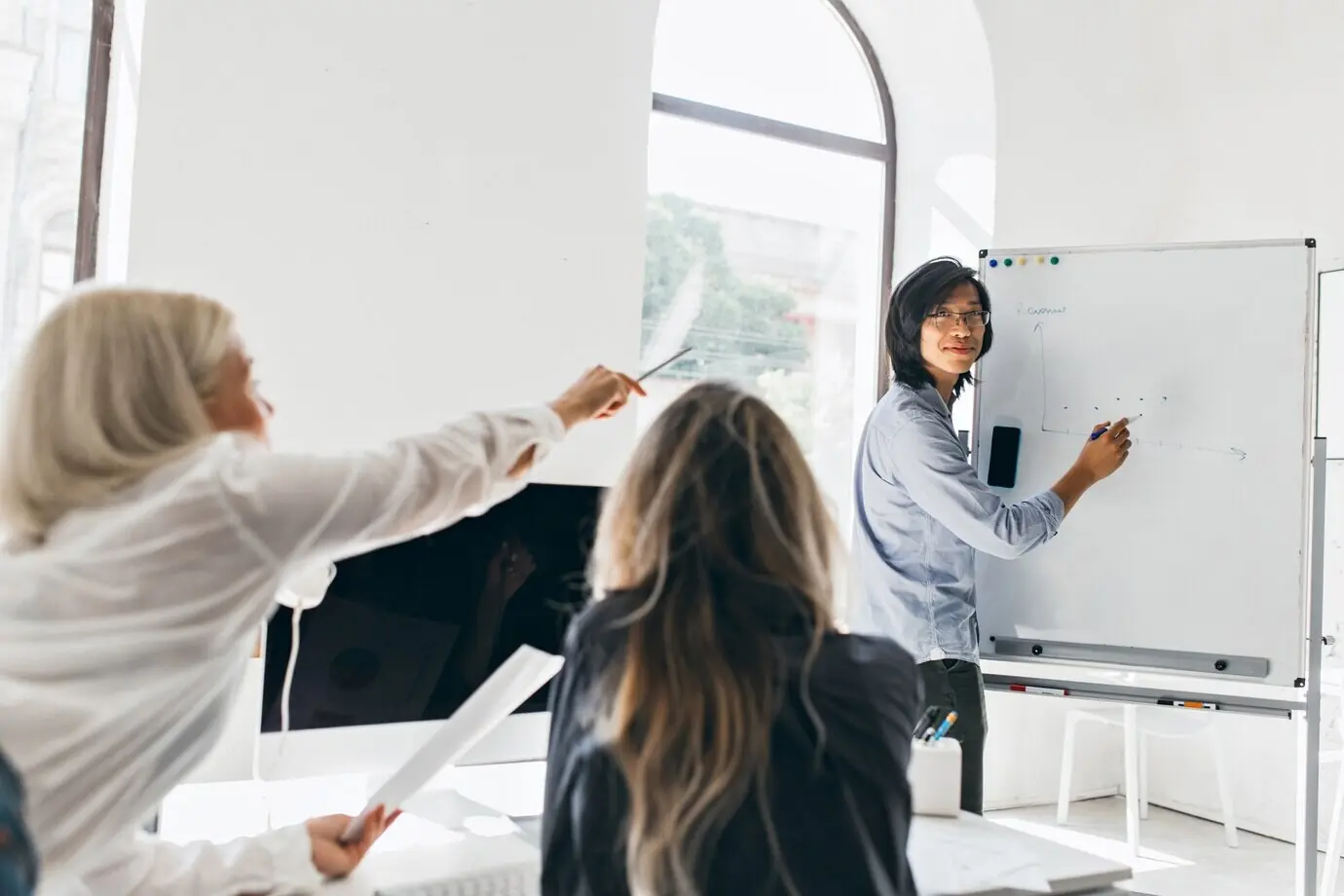 Fröhlicher junger asiatischer Mann mit Brille, der ein Diagramm auf einem Flipchart zeichnet.
